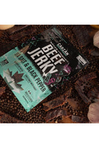 Carzan Sea Salt Black Pepper 70g beef jerky bag surrounded by peppercorns, garlic and onion, with loose jerky pieces on a wood table