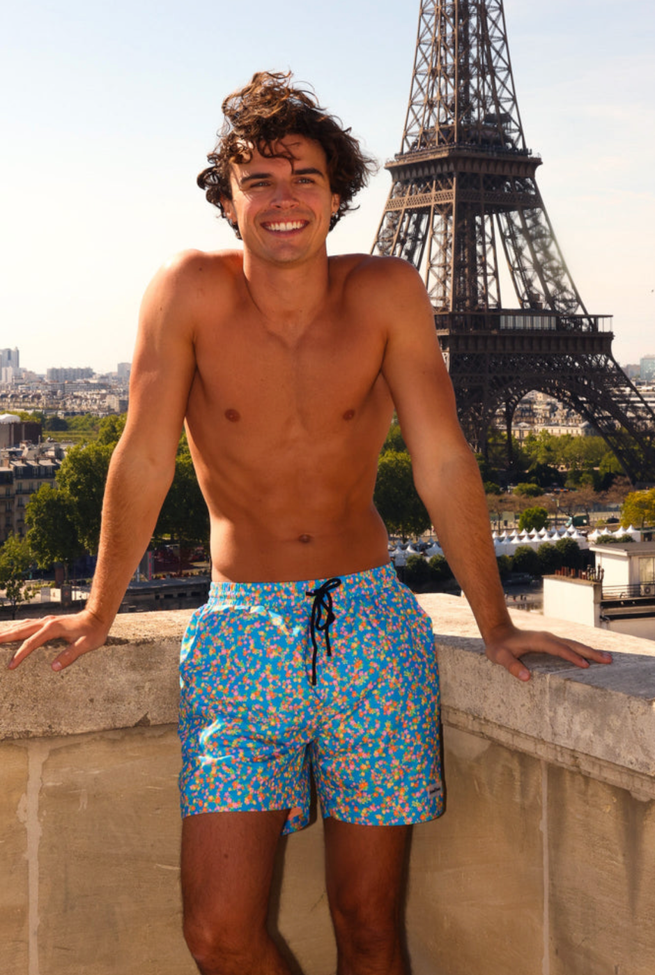 Man in swim shorts standing in front of the Eiffel Tower